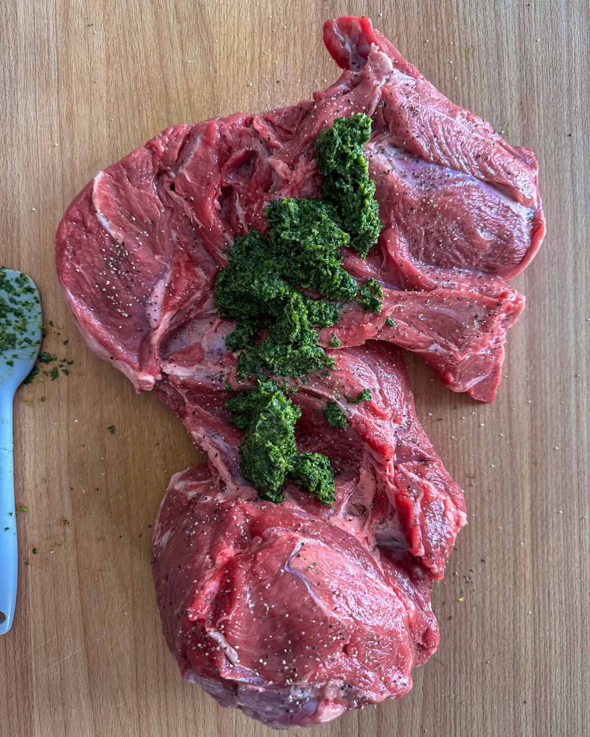Lay the boneless leg of lamb flat on a clean surface. Generously rub half of the herb sauce on the inside of the lamb.