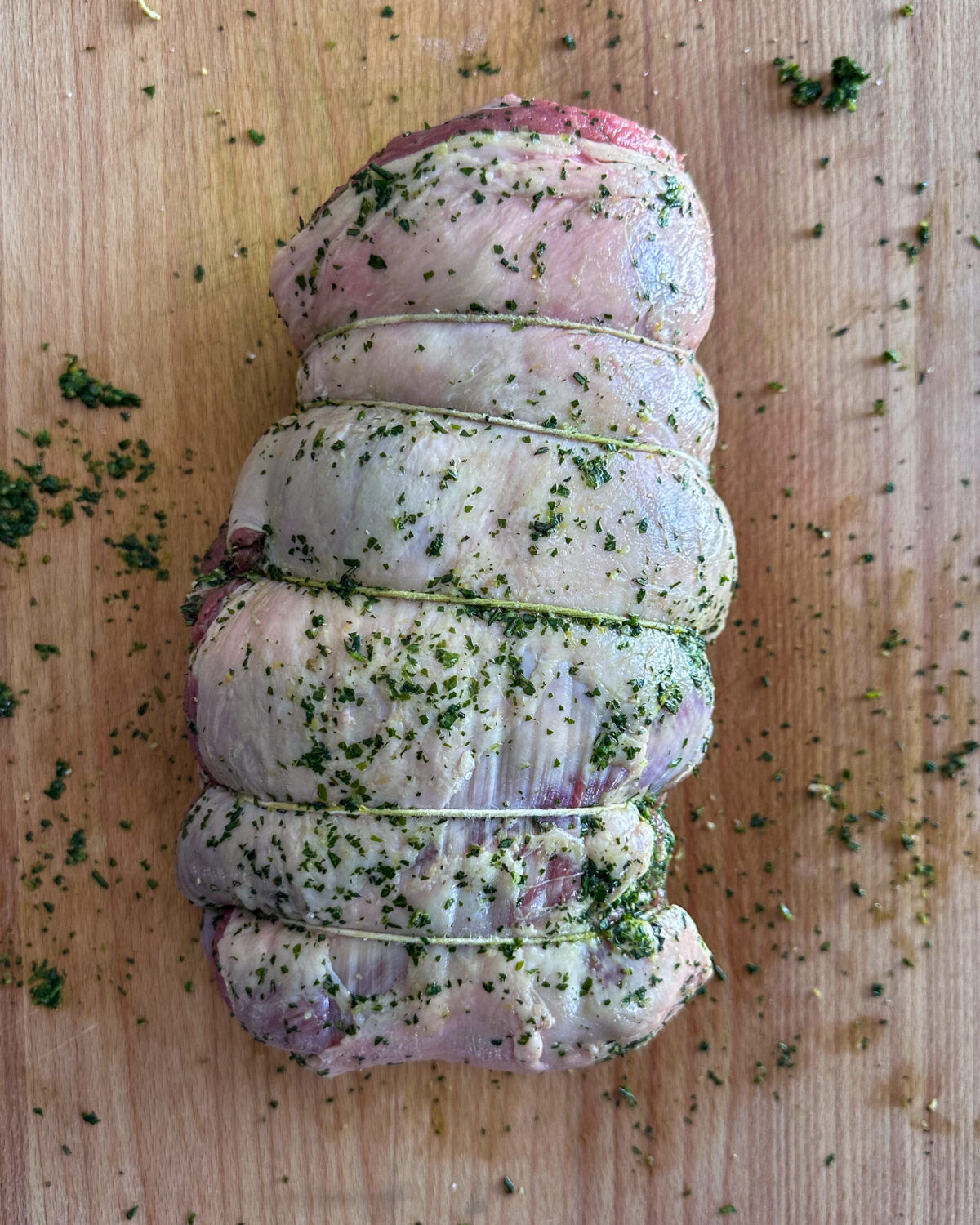 Carefully roll the lamb into a compact cylinder shape, ensuring the herb sauce remains intact inside.