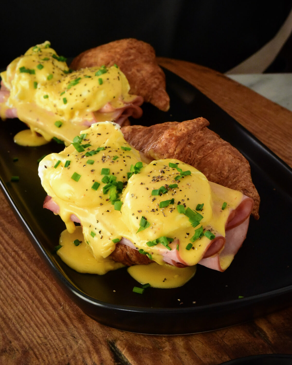 Two croissant eggs Benedict garnished with pepper and chopped chives.