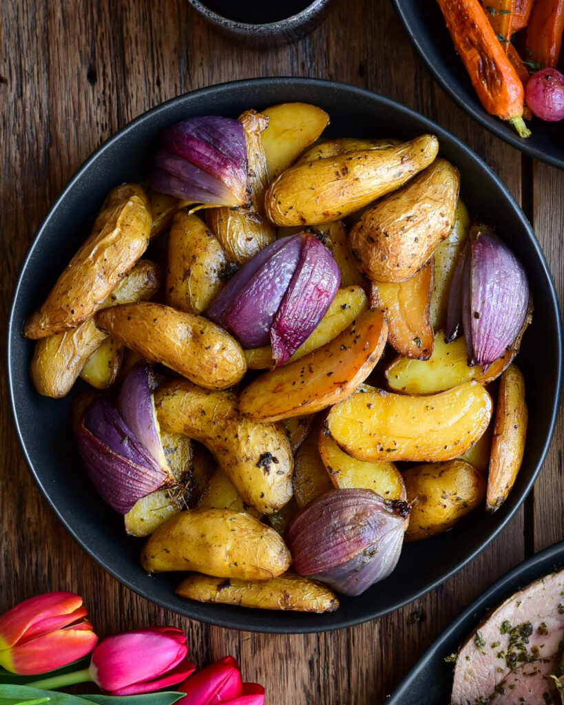 Potatoes and onions are roasted under the herb roasted boneless leg of lamb.