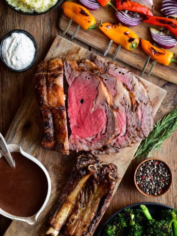 A sliced rotisserie prime rib roast served with gravy, horseradish sauce, and grilled veggies.