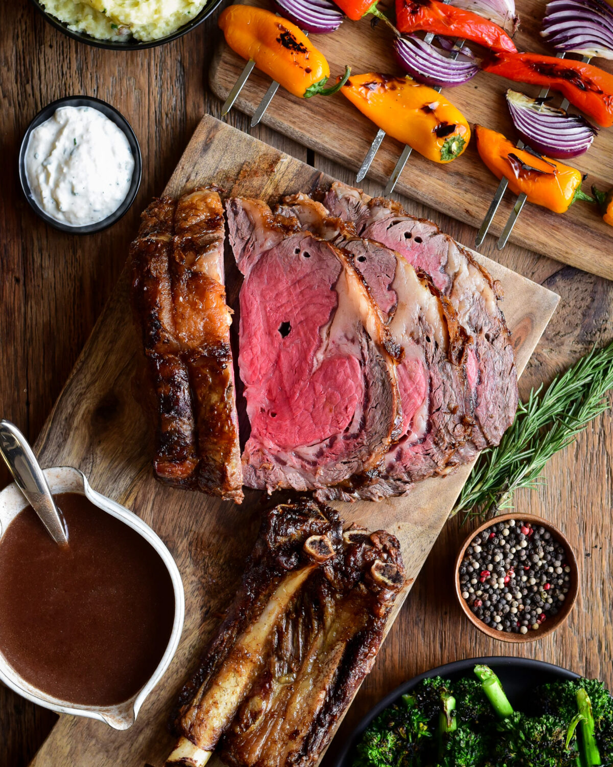 A sliced rotisserie prime rib roast served with gravy, horseradish sauce, and grilled veggies.