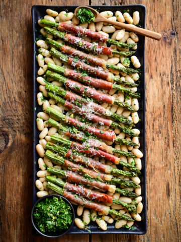 A platter with Air Fryer Asparagus wrapped Prosciutto served over a bed of cannellini beans.