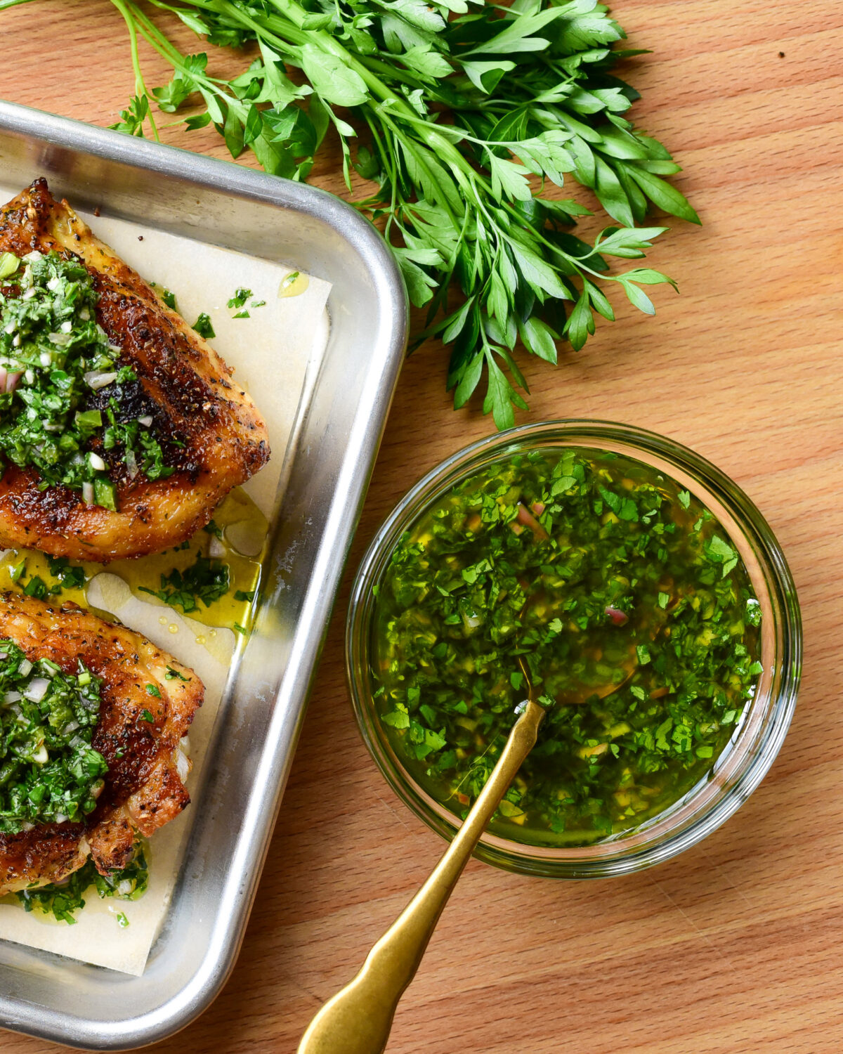 A bowl of a quick chimichurri recipe sauce with two chicken breasts and parsley.