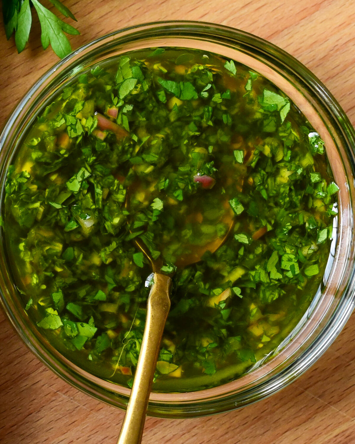 A bowl of chimichurri with a gold spoon.