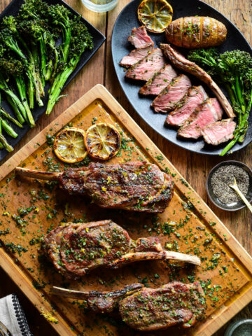 Three Tuscan style veal chops on a cutting board with sauce. A sliced chop is served with a potato and broccolini.