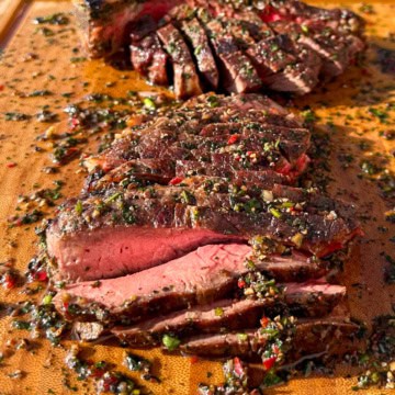 A medium-rare T-bone is sliced and on a board with a peppercorn sauce.
