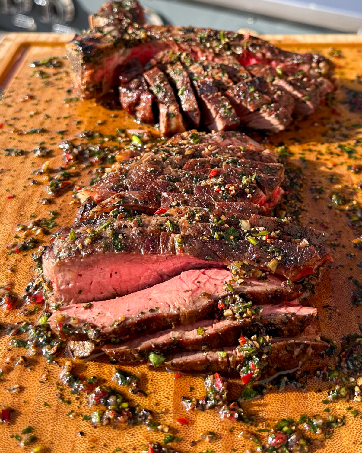 A medium-rare T-bone is sliced and on a board with a peppercorn sauce.
