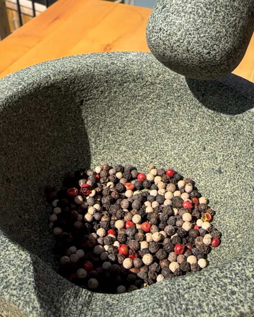 Mixed peppercorns in a mortar and pestle ready to be grinded.