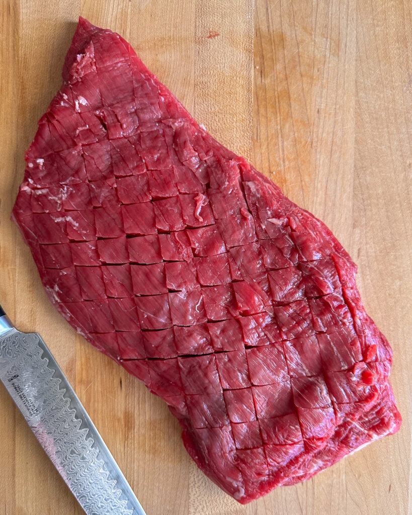 Run your knife diagonally across the surface of the flank steak, in a diamond pattern.