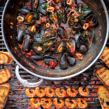 A large wok over the BBQ with Spicy 'Nduja Seafood in Tomato Broth, with shrimp skewers and baguette toasts.