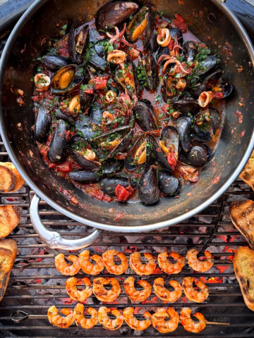 A large wok over the BBQ with Spicy 'Nduja Seafood in Tomato Broth, with shrimp skewers and baguette toasts.