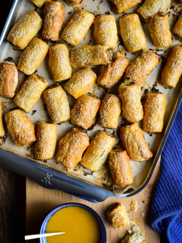 A tray of Pork, Fennel and Apple Sausage Rolls with a bowl of honey mustard dipping sauce.