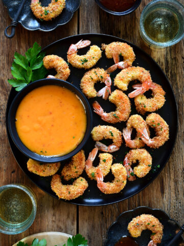A dish of with air fryer coconut shrimp and a bowl of dipping sauce.