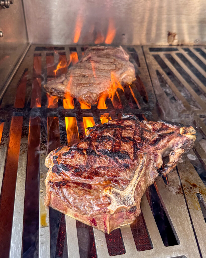 Two steaks getting seared over high heat on a grill.