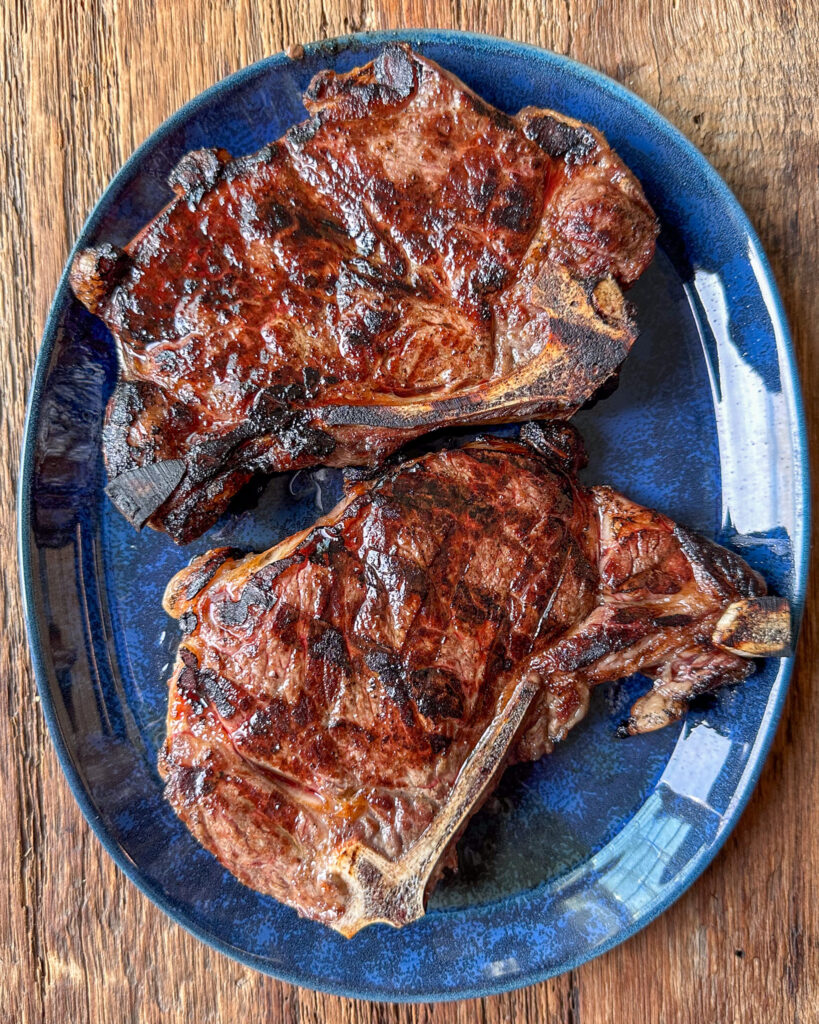 Two grilled steaks resting on blue plate.