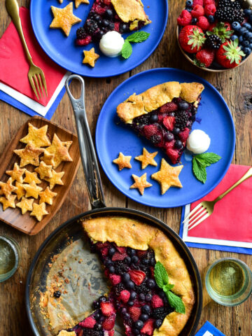 A grilled mixed berry gallet in a pan with two servings on blue plates with stars made from the crust and served with ice cream.