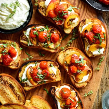 Close up of toasted garlic bread with a layer of whipped feta and topped with 3 grilled peach slices and 3 blistered tomatoes and garnished with fresh basil leaves.