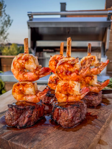 Four strip loin steaks each skewered with two shrimps and coated with teriyaki sauce.