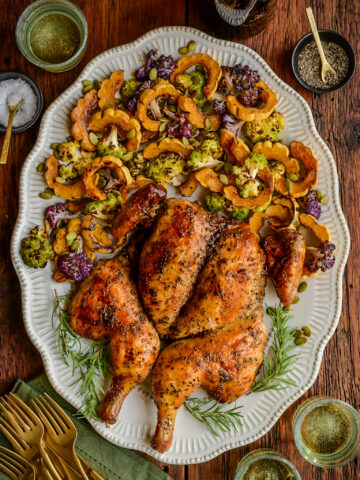 An herb butter spatchcock chicken on a platter with with roasted delicata squash and cauliflower.