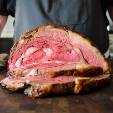A slow roasted bone in prime rib roast slice open to reveal a perfect medium rare interior.
