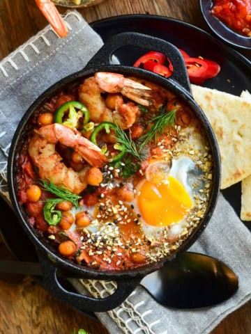 A close up of a individual shakshuka with shrimp and an egg.