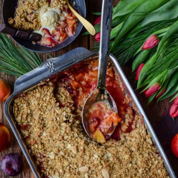 A stone fruit and cranberry fruit crisp in a baking dish with a portion served with ice cream.