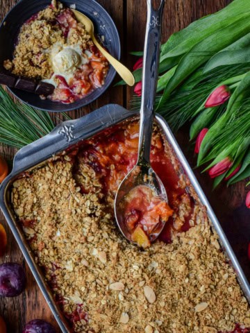 A stone fruit and cranberry fruit crisp in a baking dish with a portion served with ice cream.