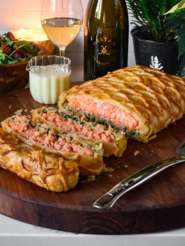 A sliced salmon en route with Leeks on a cutting board with wine and sauce.