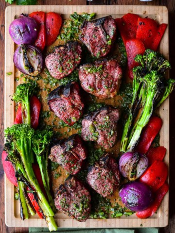 A board with grilled lamb chops with a poblano board sauce and grilled vegetables.