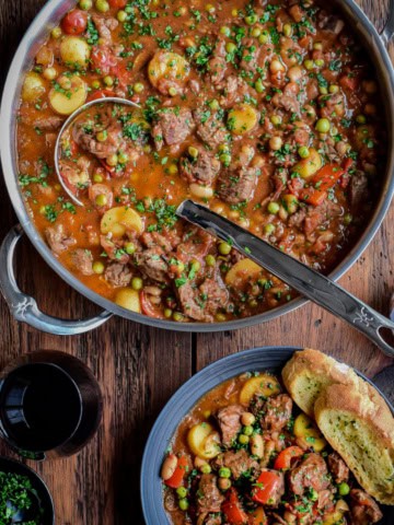 A large pot of Spanish Lamb Stew with a ladle and a bowl served with crusty bread.