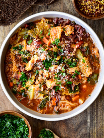 A bowl of Savoy Cabbage Roll Soup with spinach and beans. Topped with chopped parsley and grated Parmesan.