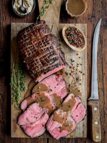 A sous vide roast beef with half of it sliced with some Marsala pepper sauce poured over top.