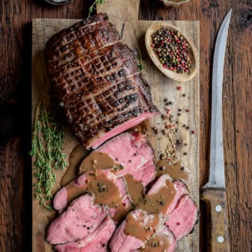 A sous vide roast beef with half of it sliced with some Marsala pepper sauce poured over top.
