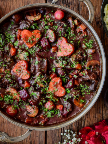 A close-up of a pot of Beef Bourguignon in a Dutch oven with root vegetables cut into hearts.