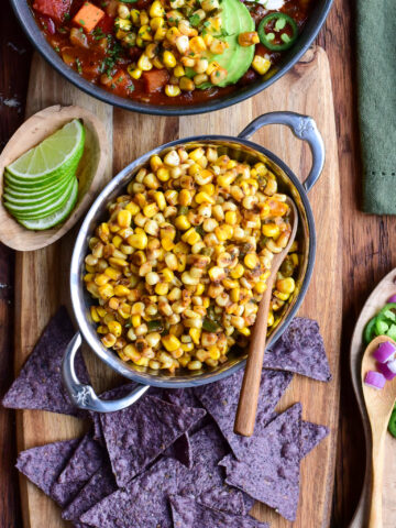 A bowl of Cajun corn served with tortilla chips, limes and chili.