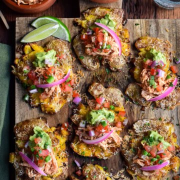 A board with Crispy Smashed Potato Tacos (or Tostadas) Topped with spiced rotisserie chicken, cheese, and fresh toppings like guacamole and Pico de Gallo,