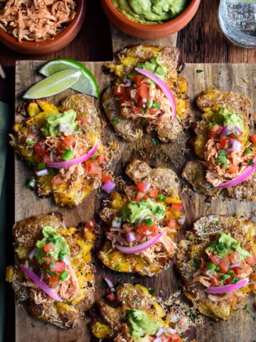 A board with Crispy Smashed Potato Tacos (or Tostadas) Topped with spiced rotisserie chicken, cheese, and fresh toppings like guacamole and Pico de Gallo,