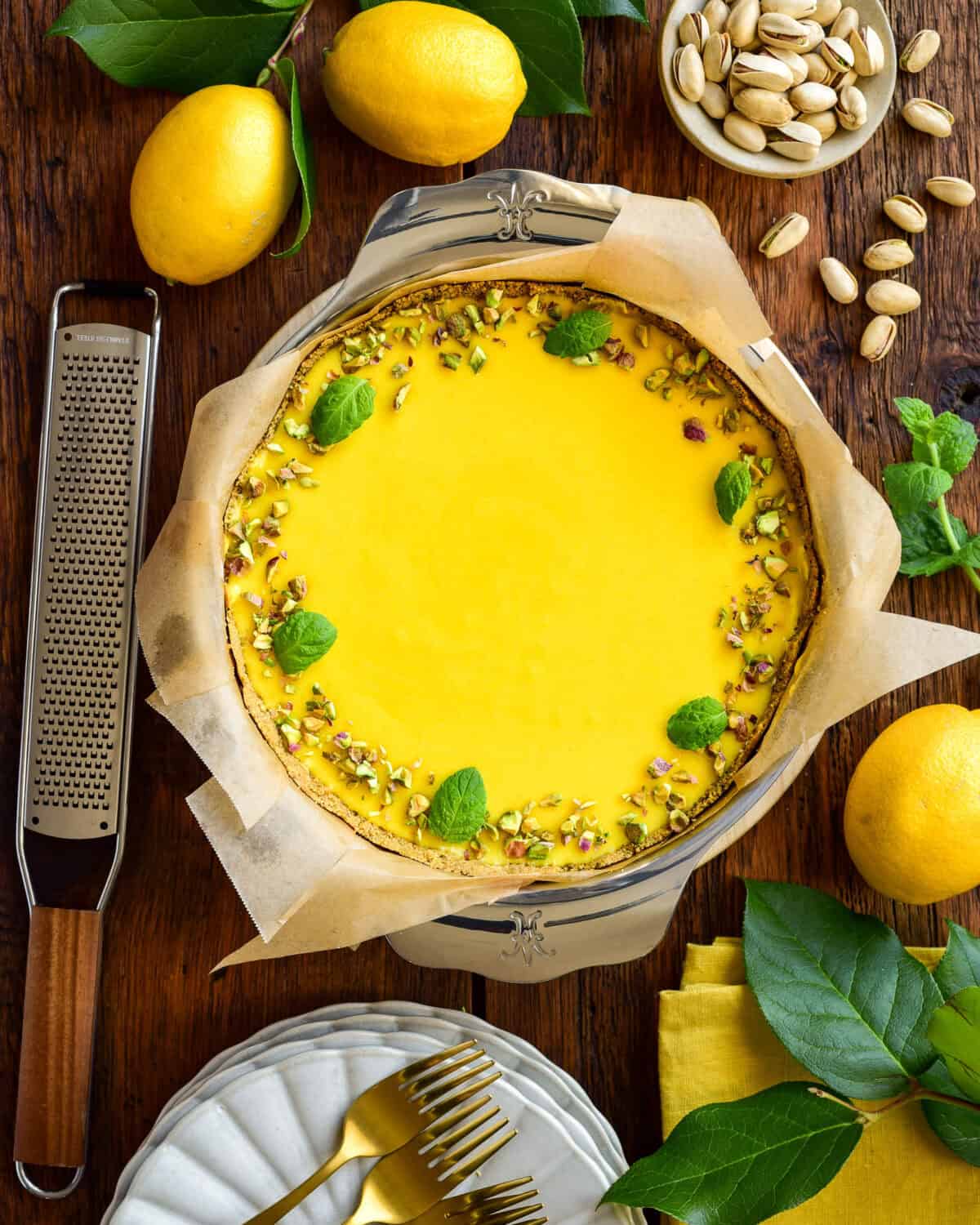 A lemon curd pie with a graham cracker crust in a pan surrounded with lemons and leaves.