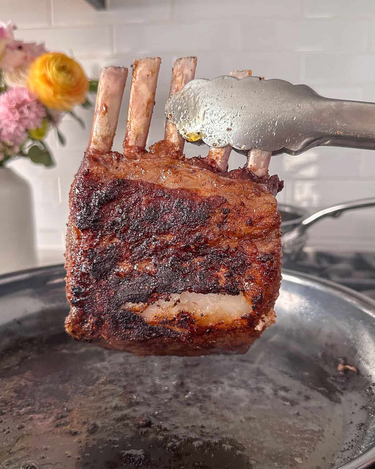 A seared wild boar rib rack lifted out from a pan.