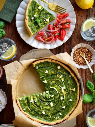 A green goddess quiche with zucchini & Feta with a piece taken out and served with a tomato salad.
