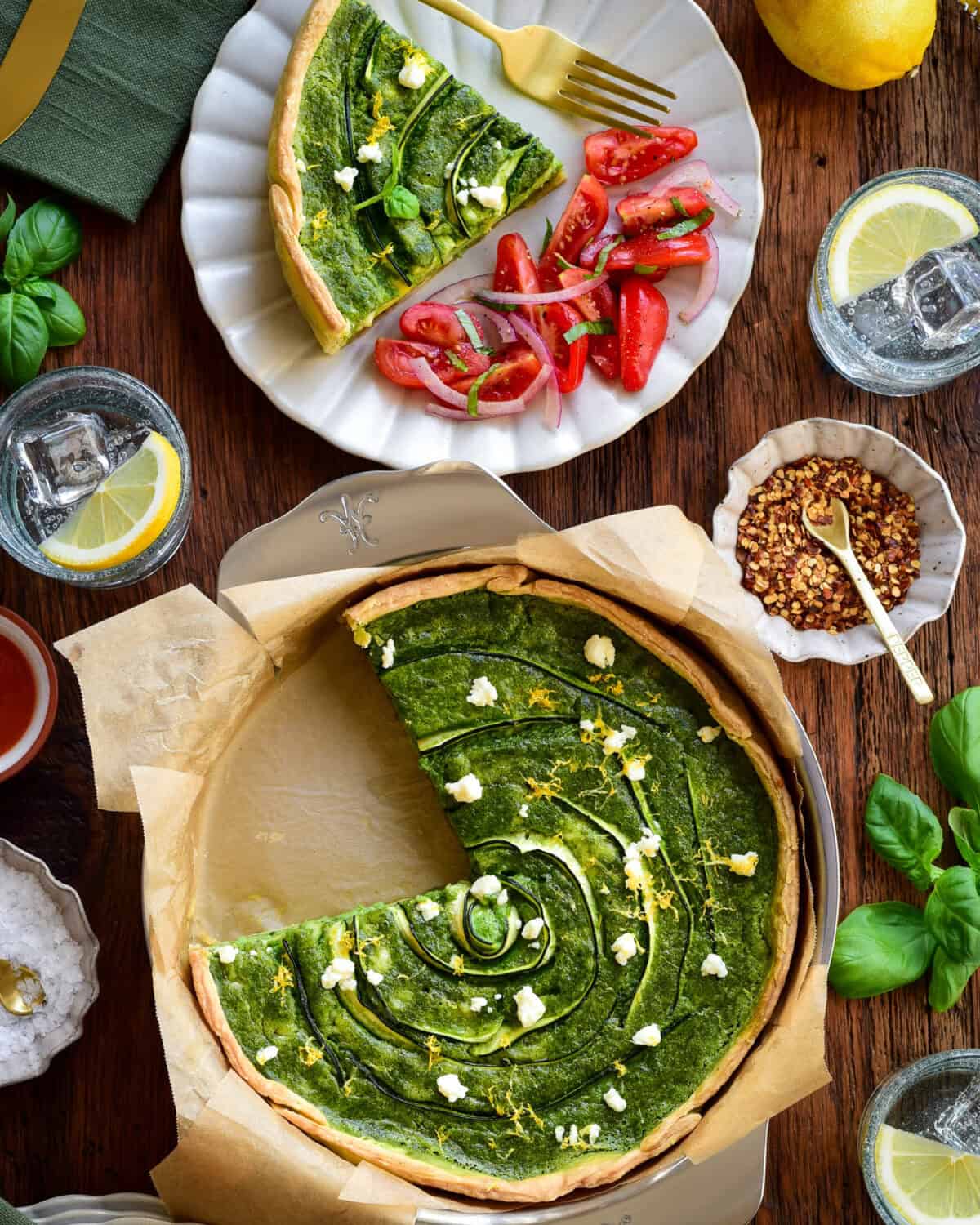 A green goddess quiche with zucchini & Feta with a piece taken out and served with a tomato salad.