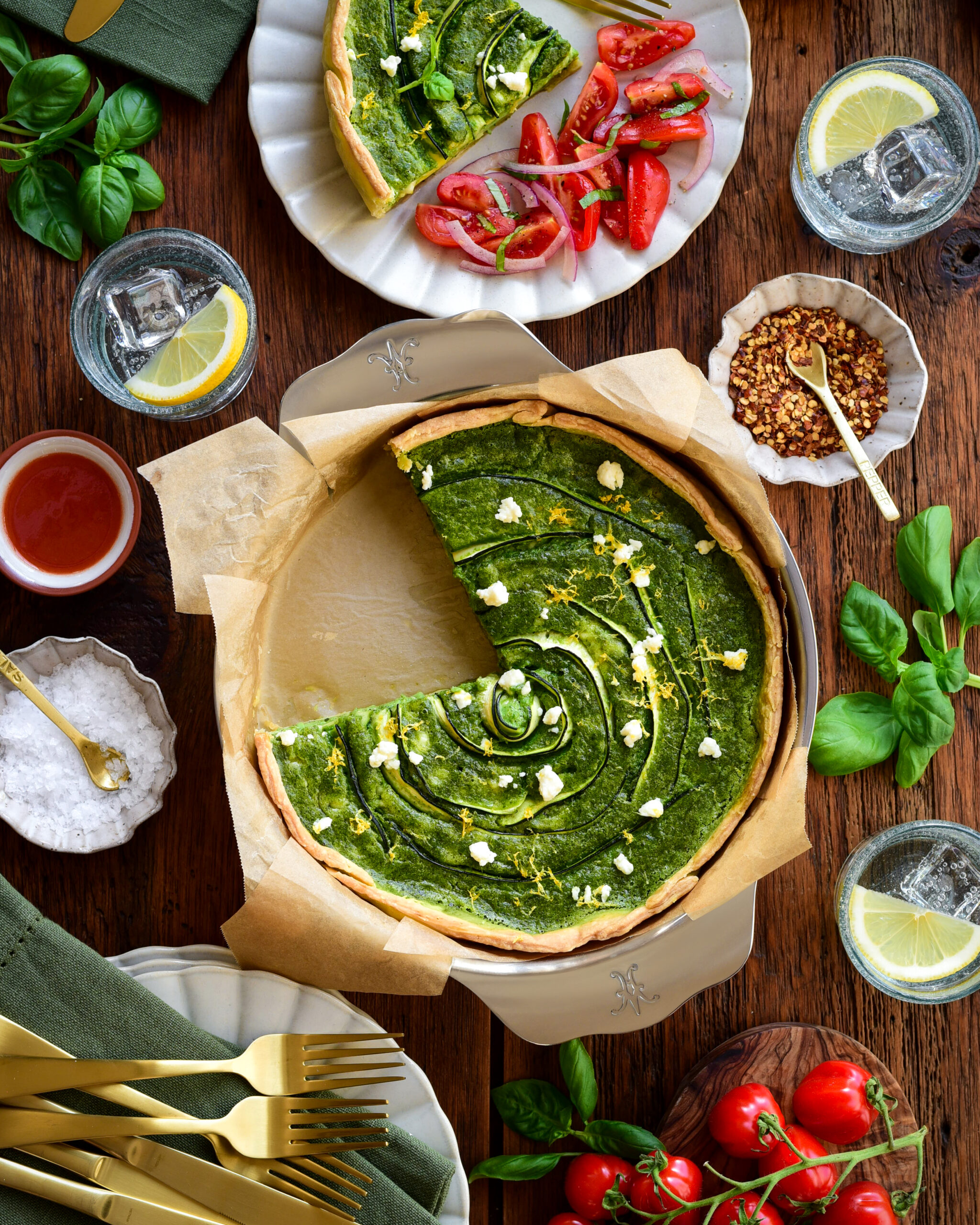 A green goddess quiche with zucchini & Feta with a piece taken out and served with a tomato salad.
