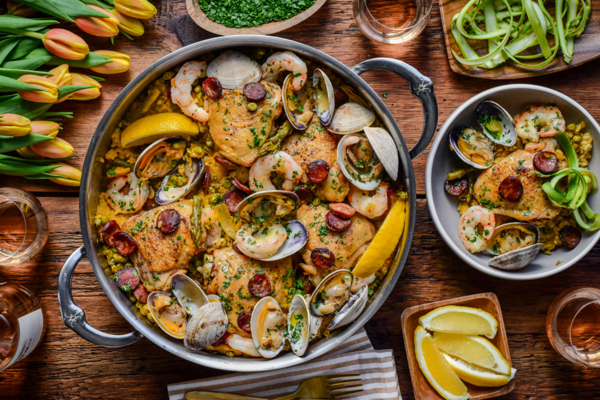 A pot and a serving of spring paella mixta with chicken, shrimp, chorizo, and clams.
