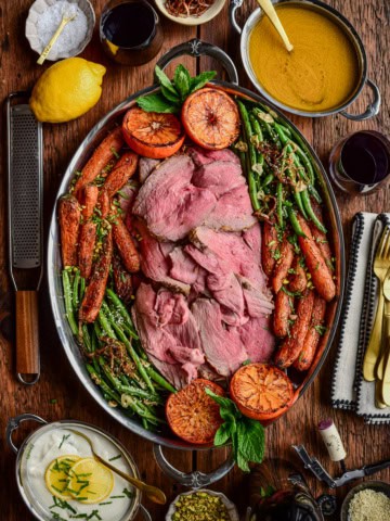 A serving platter of a Charred Citrus & Turmeric Yogurt Marinated Lamb served with carrots, green beans and charred oranges.