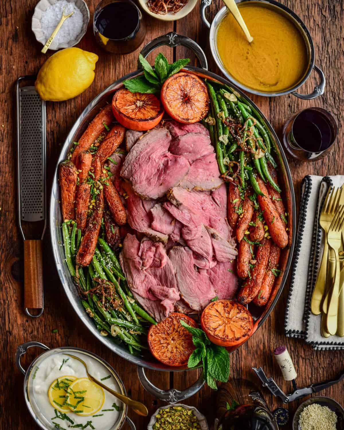 A serving platter of a Charred Citrus & Turmeric Yogurt Marinated Lamb served with carrots, green beans and charred oranges.