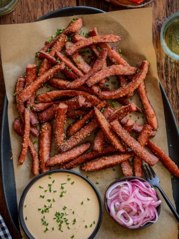 A platter of air fryer kielbasa fries with pickled onions and a spicy mustard aioli.