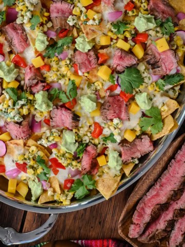 An oval platter of Carne Asada Nachos with Elote Salsa & Oaxaca Fondue served with extra steak.