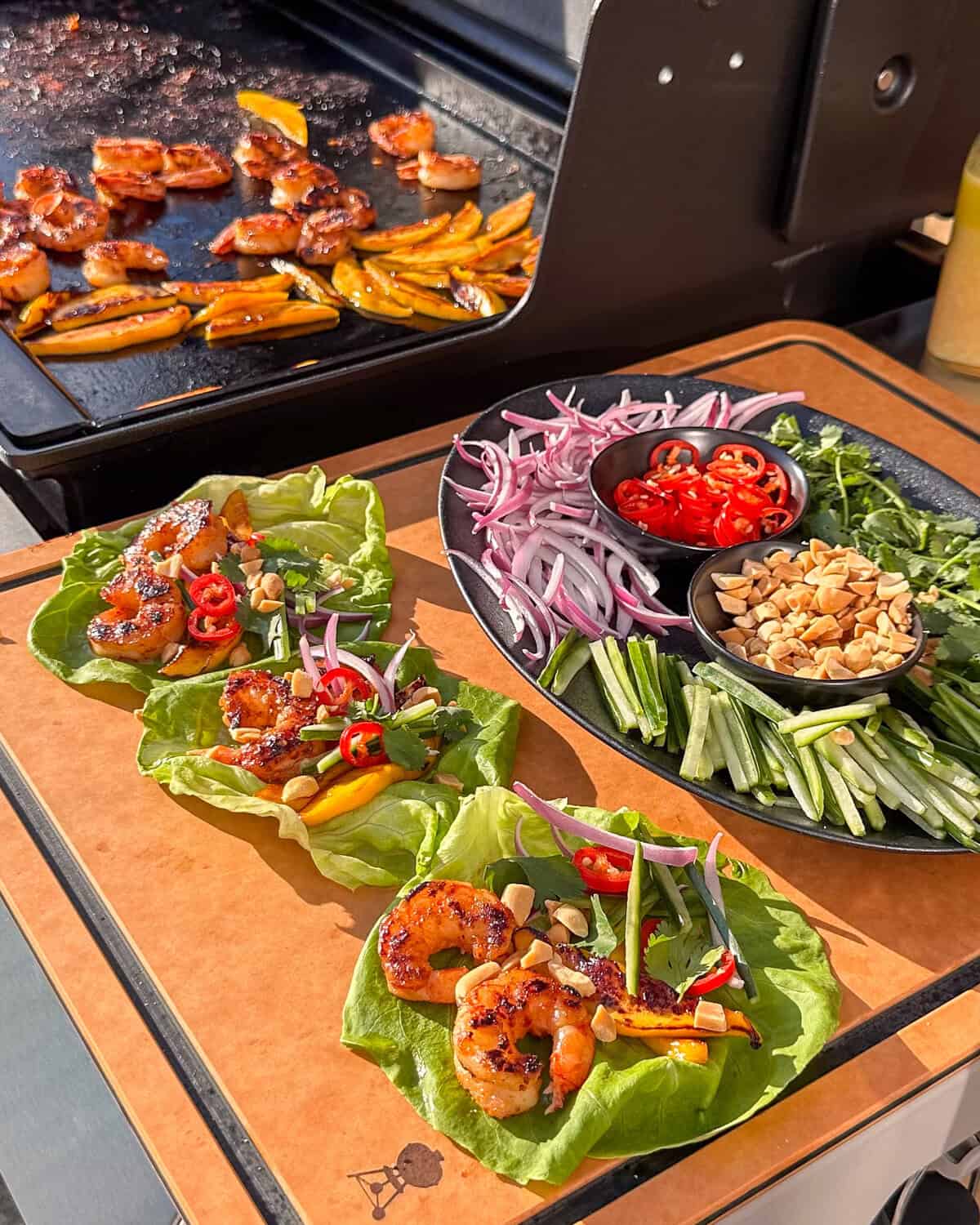 Griddle shrimp wraps on a griddle side table with toppings and extra shrimp and mango keeping warm on the griddle.