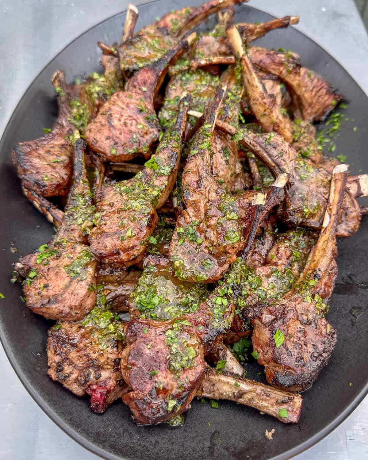 A platter of grilled lollipop lamb chops with a herb board sauce.